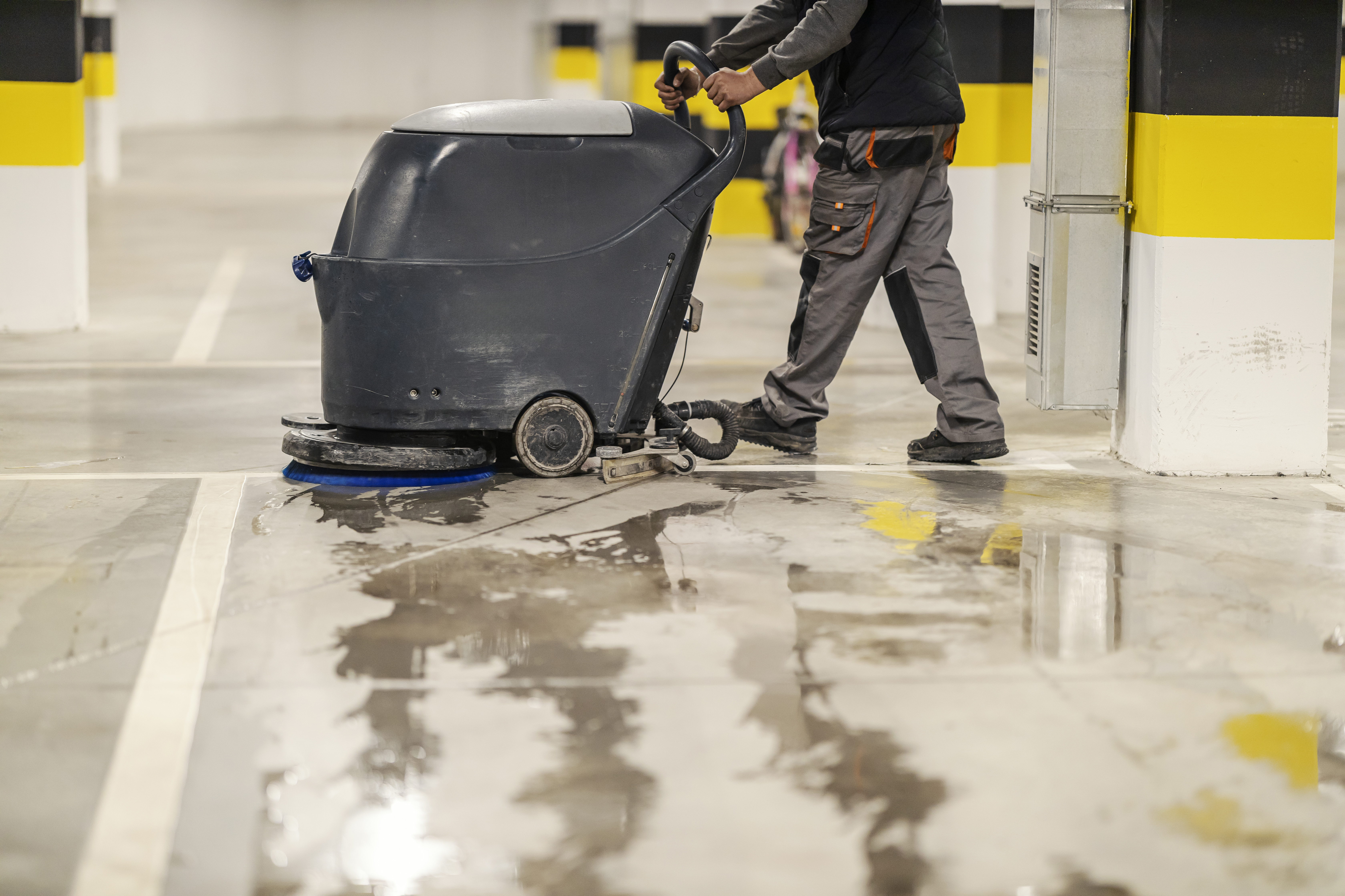 Side view of unrecognizable worker washing garage parking with washing machine.