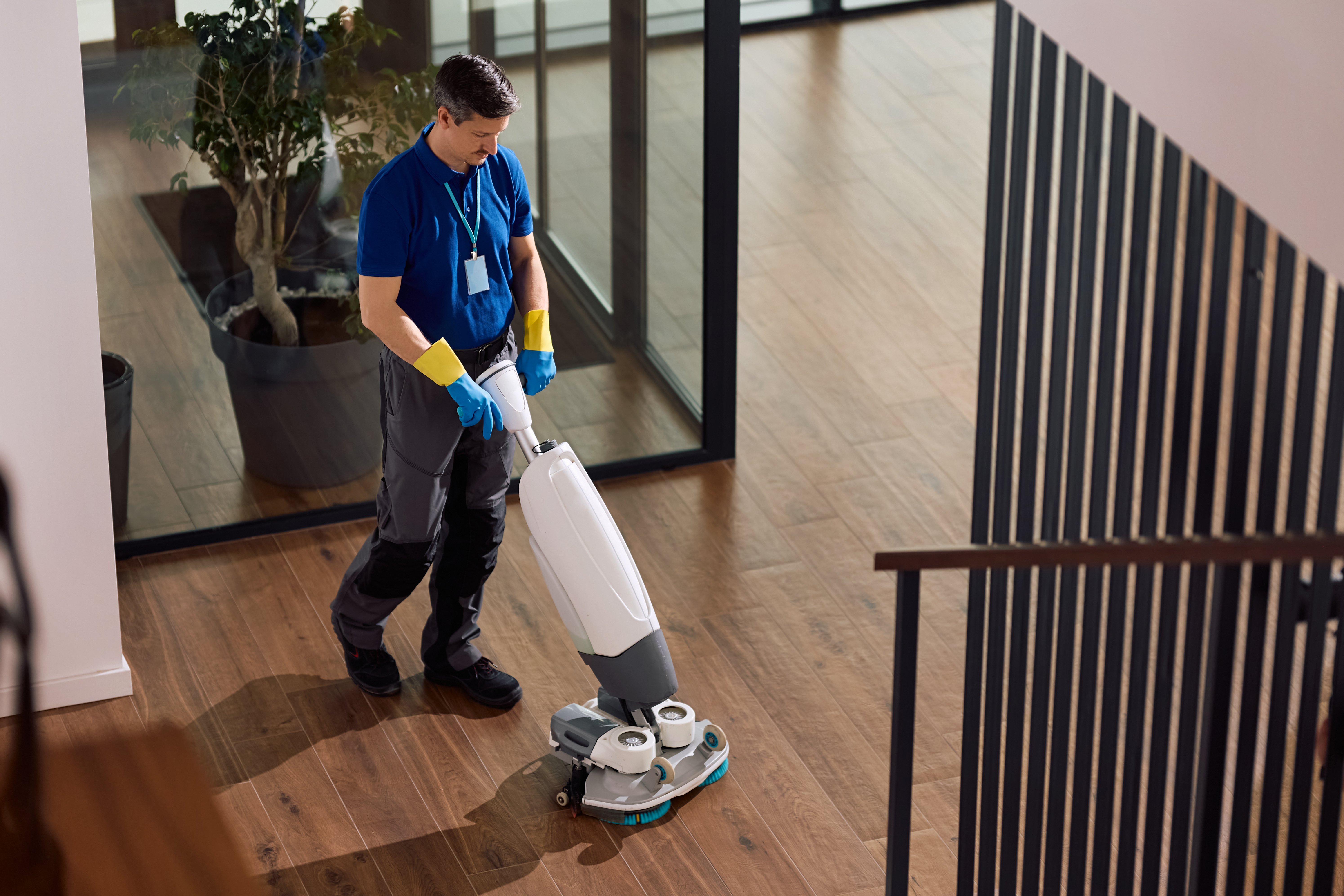 Janitorial service employee scrubbing office floors with professional machine. Copy space.