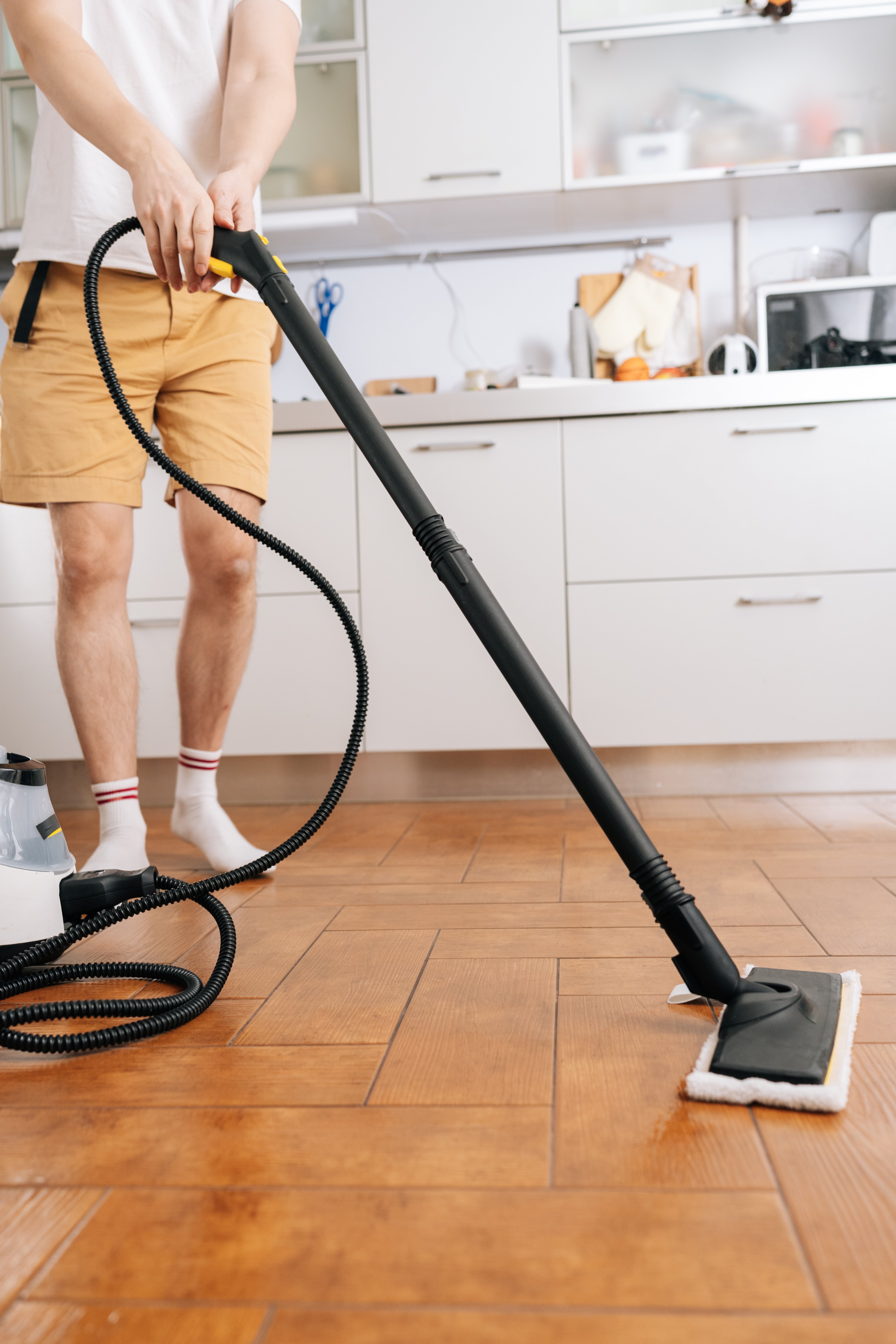 Vertical shot of unrecognizable housekeeper male using steam cleaner device to sanitize and deep clean kitchen floor, performing domestic chore for efficient home sanitation and hygiene.